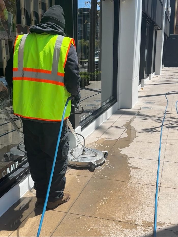 Worker using a surface cleaner along a commercial storefront sidewalk